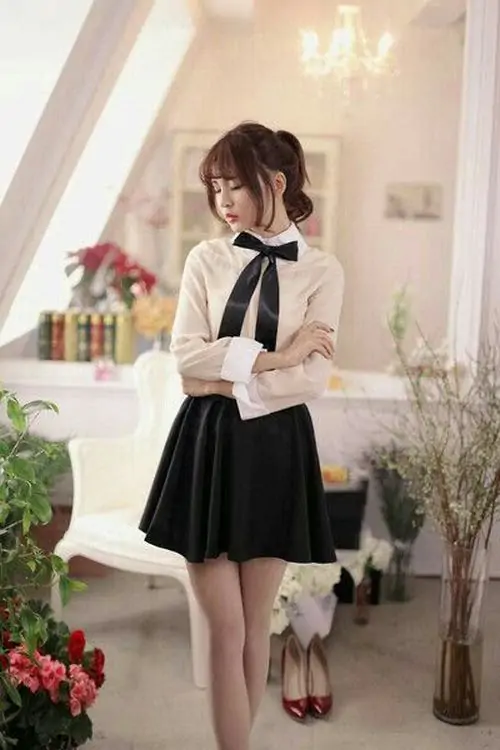 Gái xinh mặc váy ngắn đen đứng bên quán cà phê tối giản, ánh sáng vàng làm nổi bật phom dáng ôm eo