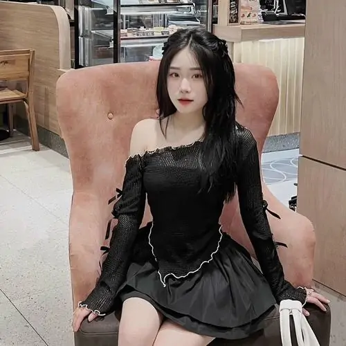 Trên ghế bành hồng, cô nàng mặc váy đen cổ vuông ngồi ngay ngắn, mái tóc dài và phụ kiện xích tạo điểm nhấn