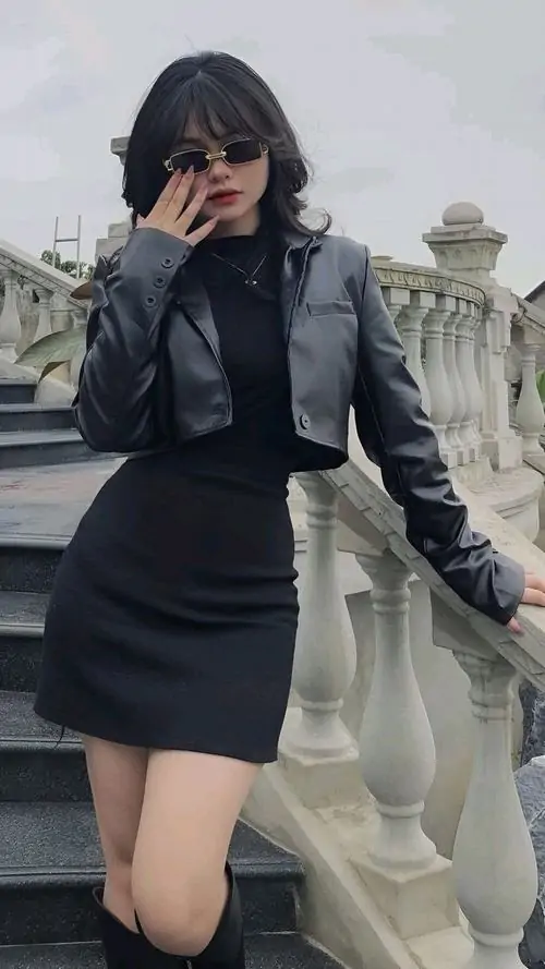 Cô gái mặc set đen đứng trên cầu thang ngoài trời, kính râm và áo khoác da tạo vẻ cá tính hiện đại
