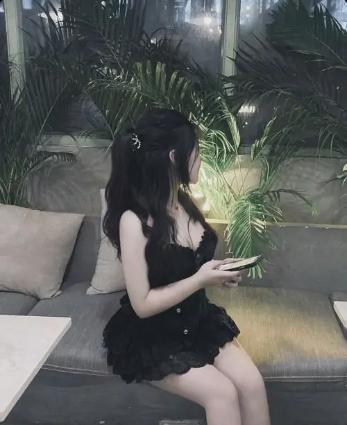 Gái xinh mặc váy ngắn đen ngồi trong góc sân vườn, tay cầm hoa nhỏ, mái tóc dài phủ vai nhìn rất nhẹ nhàng