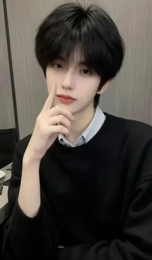 Biểu cảm trầm ngâm của người mẫu nam mặc áo len đen cổ tròn khi tựa cằm vào tay dưới ánh sáng studio nhẹ nhàng tôn lên đường nét khuôn mặt