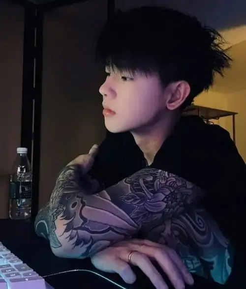 Dưới ánh đèn màu sắc mờ ảo chàng trai có mái tóc xoăn nhẹ diện chiếc áo họa tiết tối màu đang ngồi tựa lưng vào bàn đầy suy tư quyến rũ